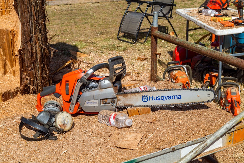 Person wearing chainsaw safety chaps, helmet, and protective gear while working near a tree