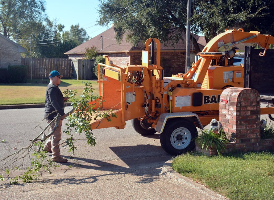 Worker feeding tree branches into a Bandit wood chipper on a suburban residential street